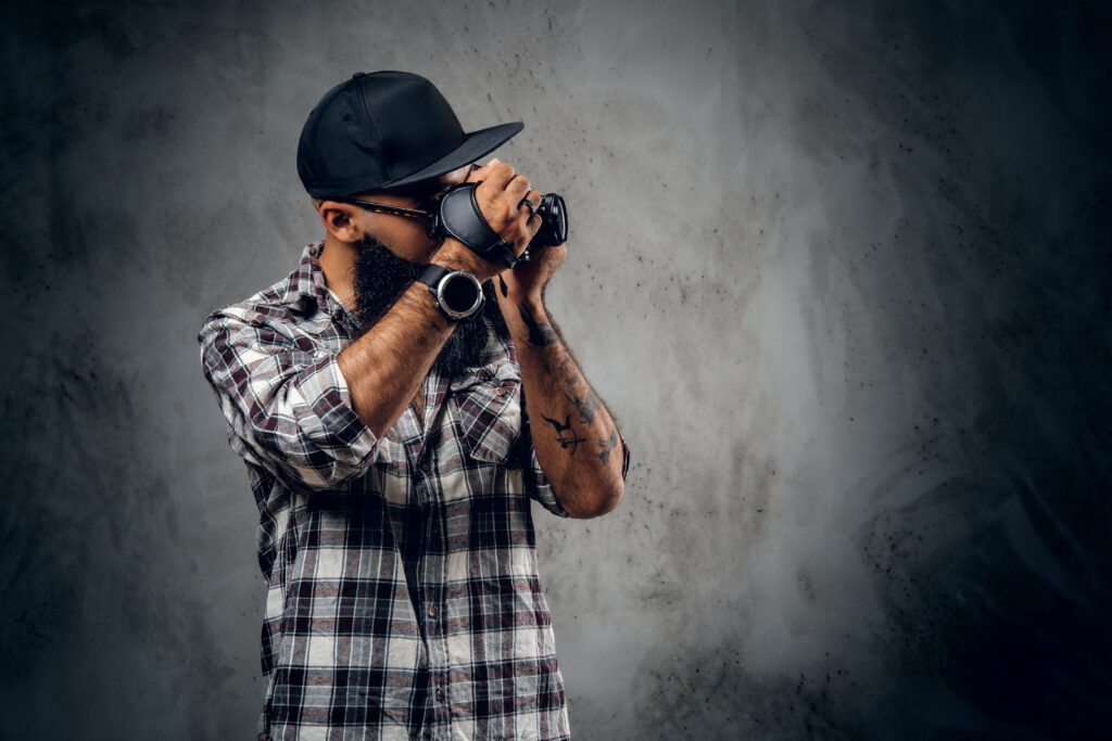 bearded hipster amateur photographer with tattoos arms dressed fleece shirt holds compact dslr camera grey background